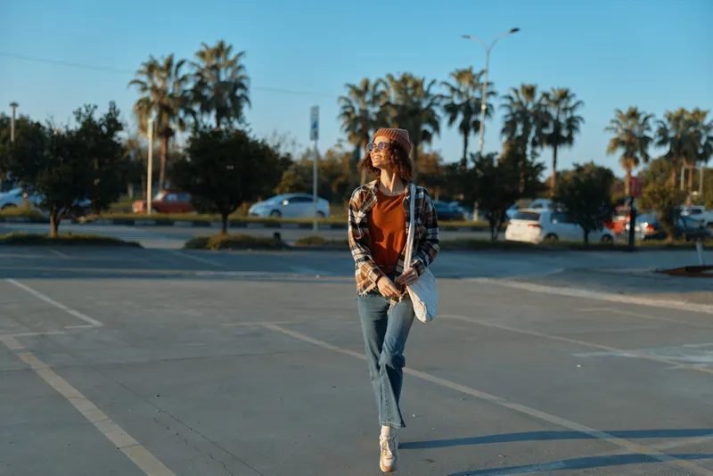 woman walking in parking lot by palms at golden hour, sunglasses on, casual jeans and jacket, authenticity and candid lifestyle captured with emotional storytelling and mindful living