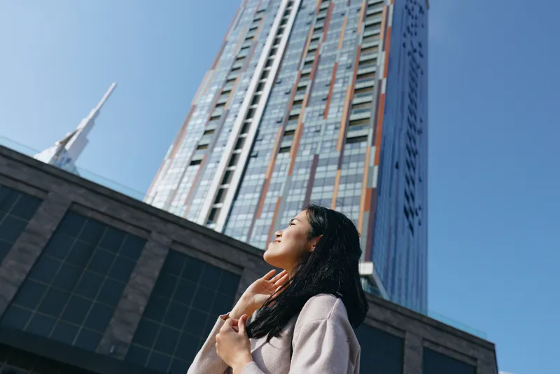 Woman gazes upward at a towering skyscraper in a modern urban landscape, captured from a low angle to emphasize ambition, discovery and city scale and perspective for storytelling