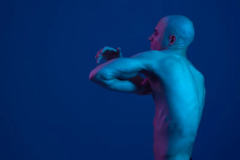 A strong man showcases his physique against a vibrant blue background, emphasizing muscularity and confidence, reflecting strength and determination in this surreal setting.