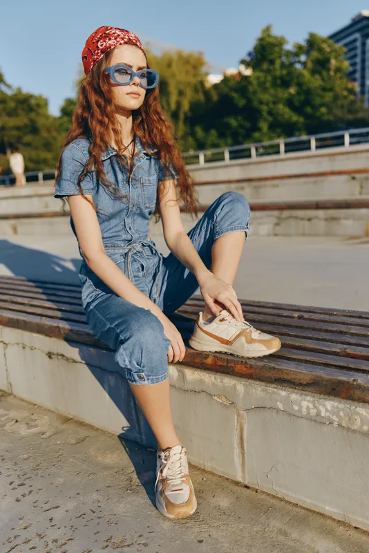 lifestyle woman in modern boho-western denim street style wearing sunglasses and sneakers outdoors with warm film color tones capturing relaxed mood
