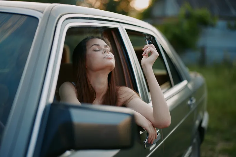 Young woman enjoying a moment of relaxation, sitting in a vintage car, exuding a carefree vibe, with natural light highlighting her emotions and casual style.