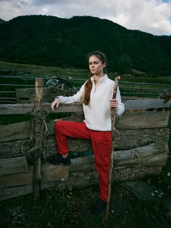 Woman, staff, fence, rural, outdoor, mountains, countryside, landscape: a calm, determined scene as she stands beside a weathered gate in a green valley.