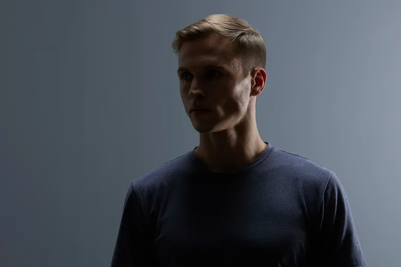 thoughtful man in shadow dark moody portrait wearing dark t-shirt looking down on black background low key lighting artistic photo