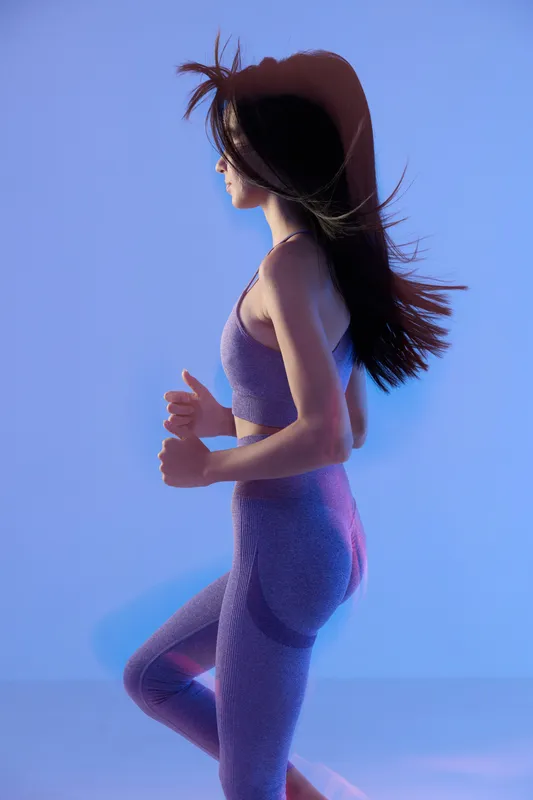 woman sport fitness running in seamless purple activewear, dynamic side profile with flowing hair, illuminated by soft blue lighting, energetic and focused pose