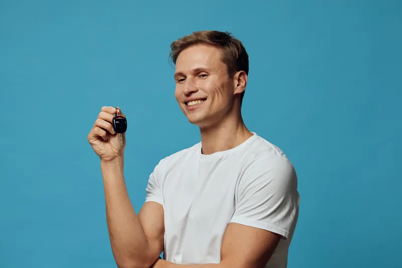 smiling young man holding smart car key remote device isolated on blue background casual wear technology concept smiling man automotive digital key security