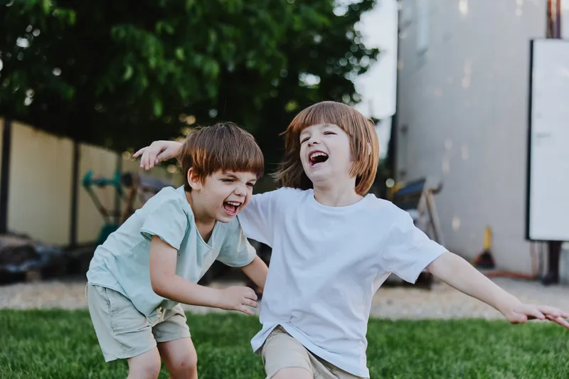 Joyful boys playing together in a sunny backyard, laughing and enjoying childhood moments with vibrant greenery surrounding them.