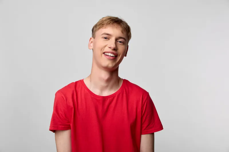 Smiling, young man in a red shirt in a studio setting conveys casual confidence, approachability, and modern lifestyle appeal suitable for fashion, advertising, and social campaigns.