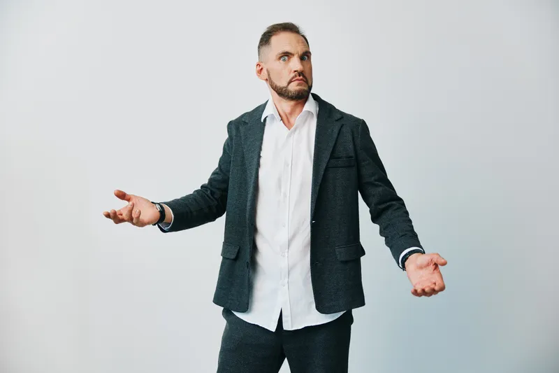 Portrait of a business professional man with open arms, emotional gesture, standing against an isolated colored background. This moment conveys curiosity and inquiry in a confident pose.