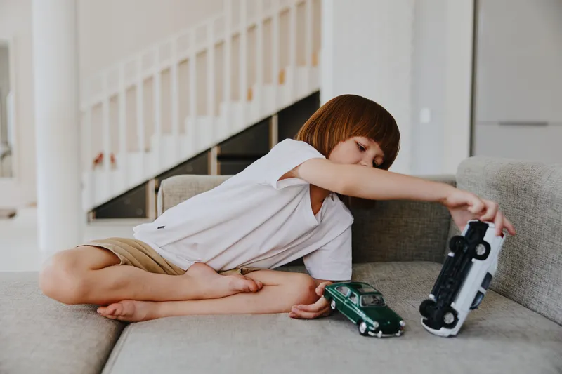 Playful boy engaging with toy cars on a cozy sofa, showcasing creativity and imagination during playtime. Bright indoor setting emphasizes a joyful atmosphere.
