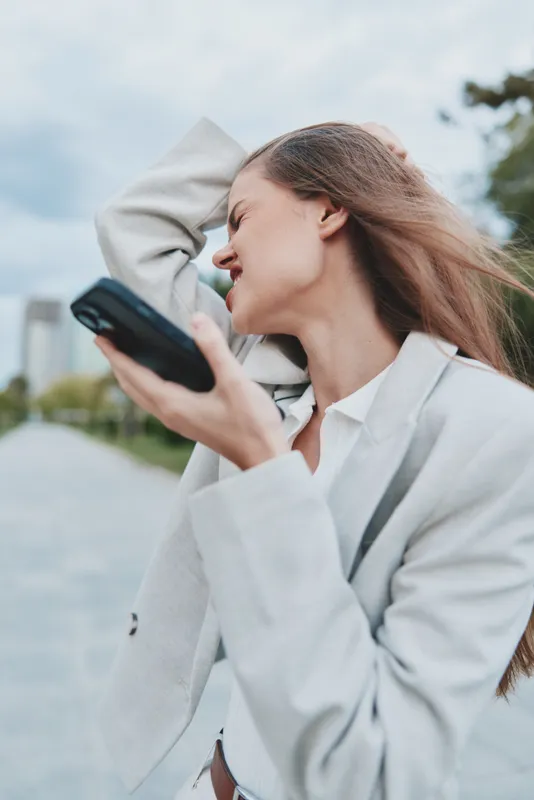 frustrated young woman holding phone outdoors feeling stress and disappointment in business casual jacket