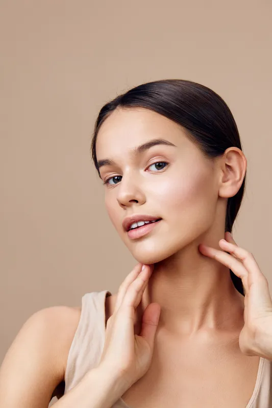 Beautiful young woman with smooth skin and natural makeup, showcasing a skincare routine, against a soft beige background, emphasizing natural beauty and confidence