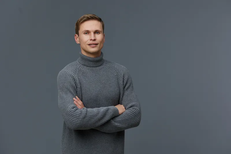 Young caucasian man standing crossed arms wear gray knitted sweater looking camera on neutral gray background portrait confidence digital nomad concept