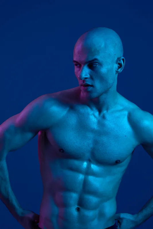 Athletic man posing under dramatic blue lighting, showcasing a fit physique and strong features, creating a captivating visual impact in a striking color palette.