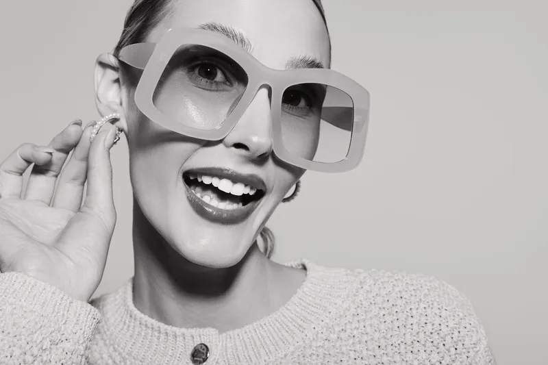 Happy young Caucasian woman with pale skin wearing oversized sunglasses smiles widely. Studio portrait with clean background. Concept for fashion, joy, and positive emotions.