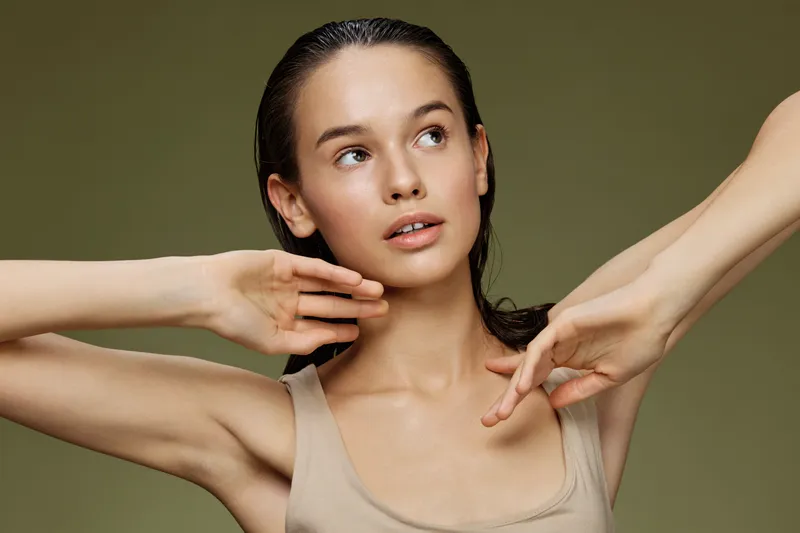 Elegant young woman with natural makeup and wet hair posing gracefully, conveying confidence and serenity against a soft green background