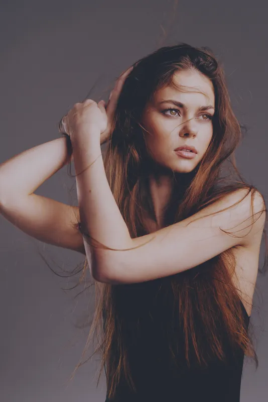 portrait of a thoughtful woman with long brown hair against gray background in soft light