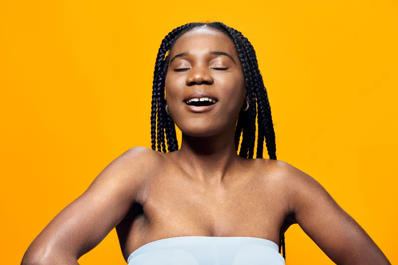 Joyful African woman with braided hair smiling against a vibrant yellow background, embodying happiness and positivity in a summer themed concept