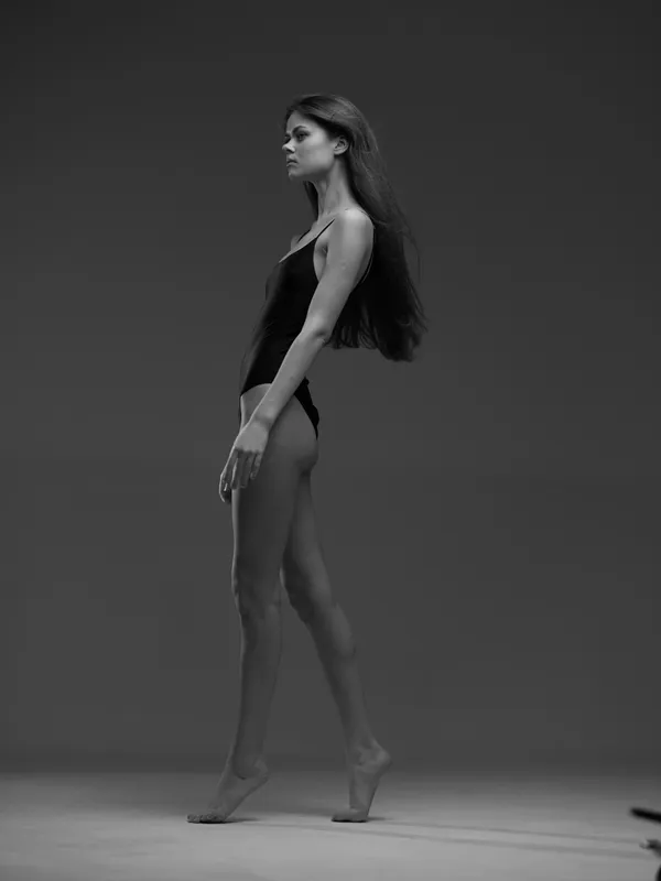 Black and white portrait of a slender woman in minimal clothing posing confidently with long hair.