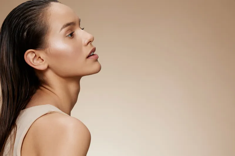 Profile of a young woman with wet hair, showcasing natural beauty against a beige background, perfect for skincare and beauty concepts