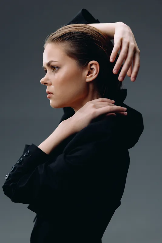 Profile of a thoughtful woman in black clothing with a dark background and soft lighting