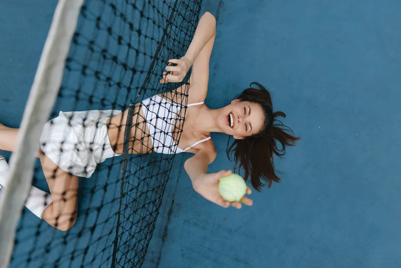 Energetic young woman playing tennis with a tennis ball, smiling and enjoying the game on a blue court, embodying a sporty lifestyle and vibrant energy