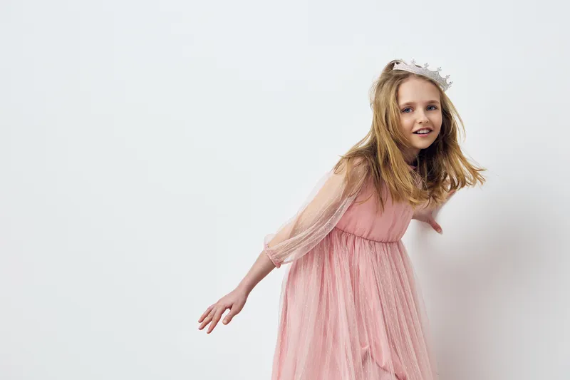 Joyful young girl in a pink dress with a crown, expressing happiness in a minimalist studio setting, perfect for children s fashion and portrait photography