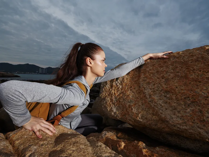 Young woman climbing rocks during outdoor adventure, expressing determination and strength in a natural coastal setting