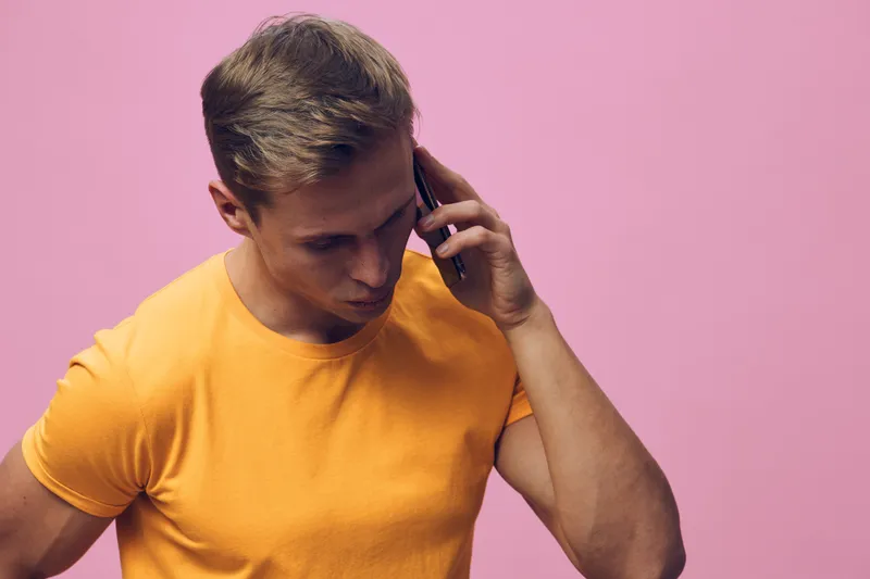 young man talking phone in orange t-shirt on pink background communication digital nomad technology modern lifestyle concept