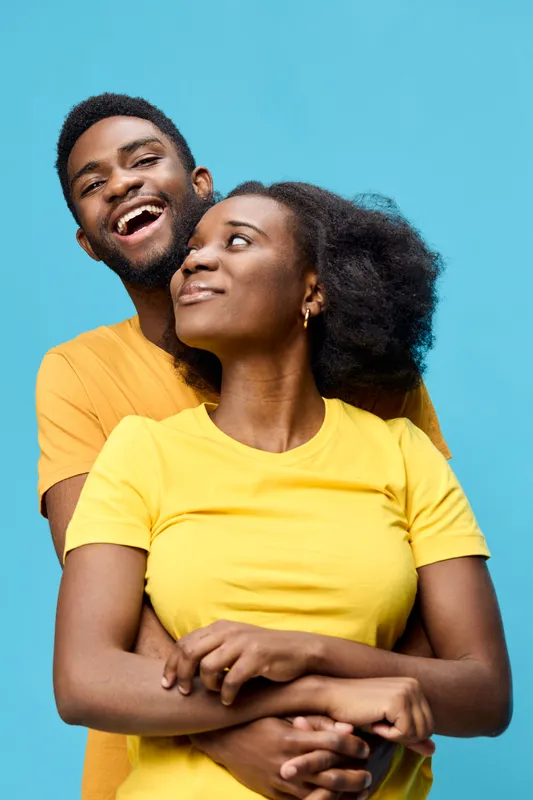 Happy diverse couple embracing against a bright blue background, wearing matching yellow t shirts, showcasing joy and love in a modern, vibrant lifestyle concept