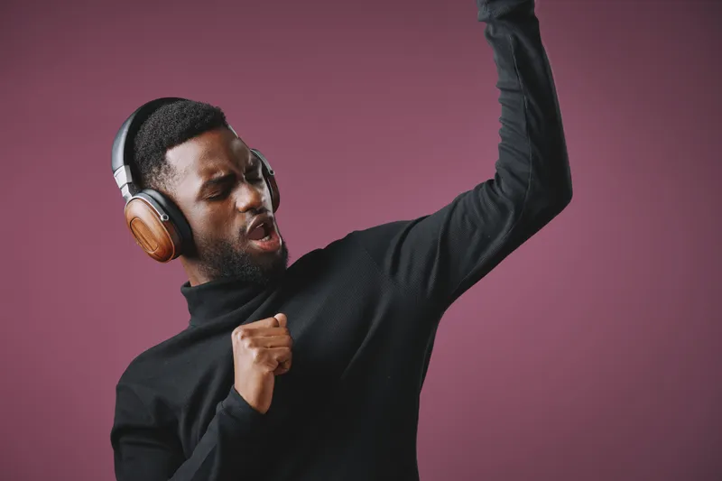 Young African man enjoying music with headphones, expressing joy and energy against a purple backdrop Stylish black turtleneck enhances the vibrant atmosphere