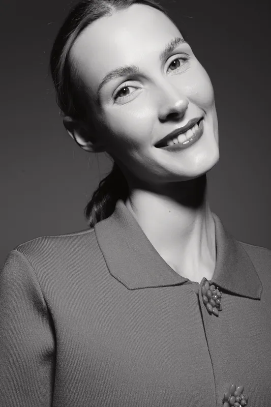 Portrait of a smiling young Caucasian woman with fair skin and tied hair wearing a textured coat. Studio lighting highlights natural beauty and joyful facial expression.
