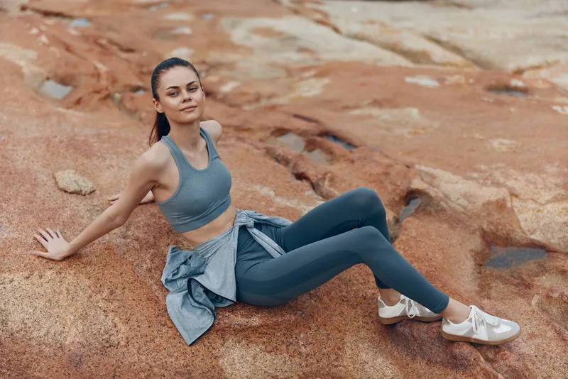 Young athletic woman in sportswear sitting on rocky terrain, exuding confidence and serenity, representing active lifestyle and fitness