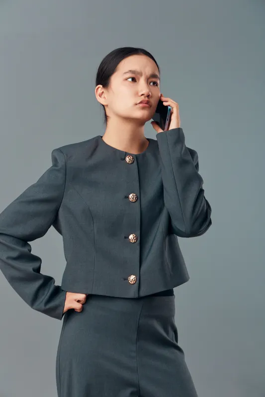 Businesswoman with serious expression talking on phone in gray suit standing isolated on light background. Professional female employee communicating for work or important conversation.