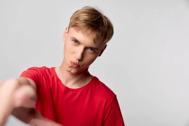 Playful young man in a red shirt points at the camera with a puckered lips expression, creating a bold energetic shot suitable for social media, lifestyle, or marketing visuals.