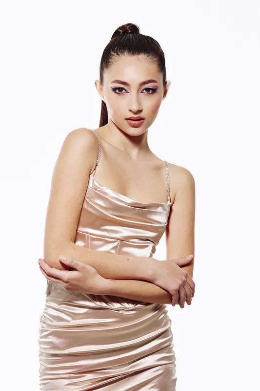 Young woman with smooth pink satin dress and creative makeup poses confidently against white background. Fashion and beauty concept with modern style.