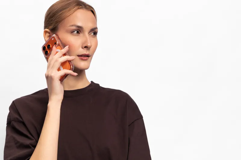 Young woman in black shirt holds smartphone near ear looking thoughtful isolated on white background. Concept for communication, technology, conversation, and modern lifestyle.