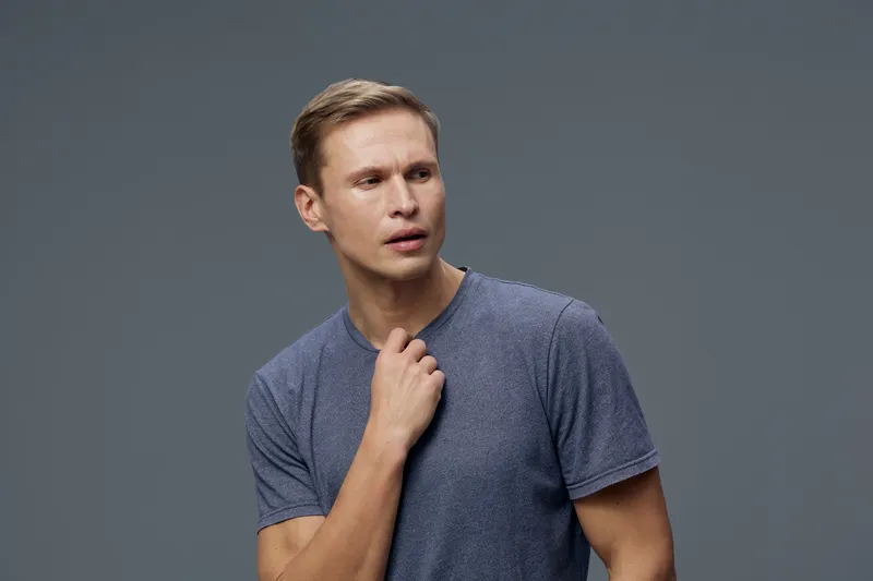 thoughtful caucasian man with short hair wear grey t-shirt look away touch neck isolated on grey background studio portrait mental health gadgets concept