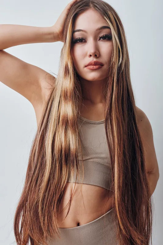 Young woman with long straight hair posing in beige crop top and pants against white background. Casual style, beauty portrait with natural makeup and confident look