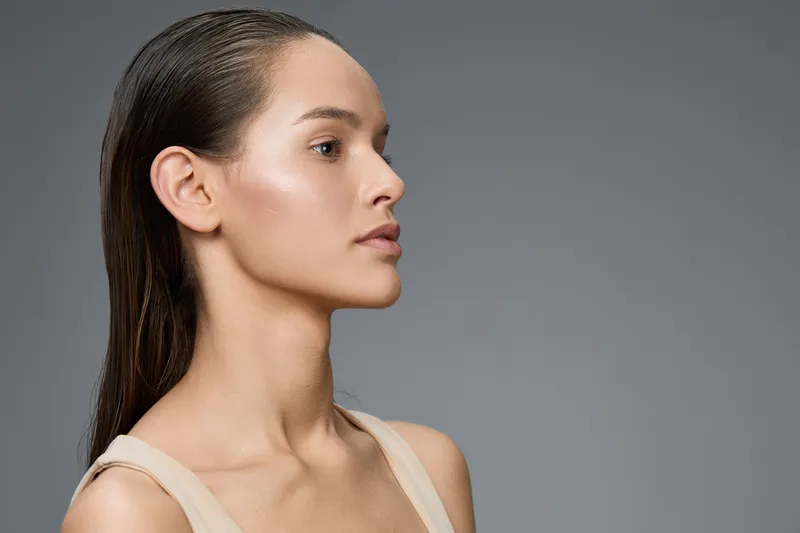 Profile portrait of a beautiful young woman with long hair, showcasing natural beauty and elegance against a minimalistic gray background, emphasizing healthy skin and modern style