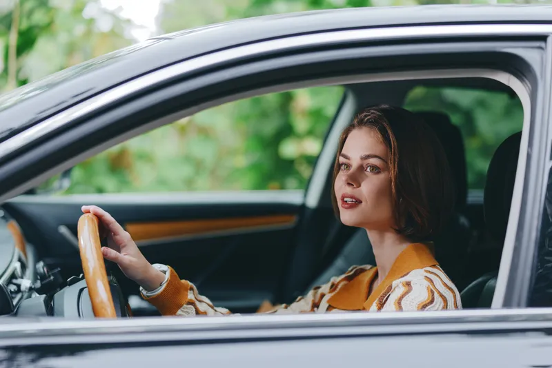 Car, driver, woman, smile a cheerful woman sits inside the car, hands on the steering wheel, calm expression, bright mood, confidence, joy, readiness for a journey in the vehicle