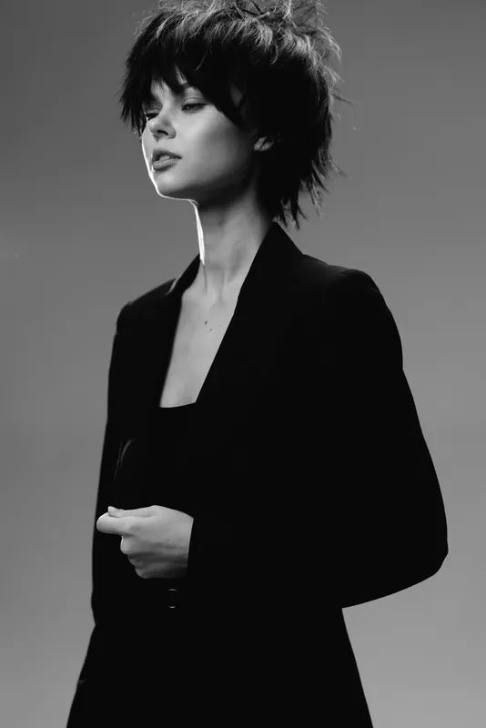 Black and white portrait of a young woman with short hair wearing a dark blazer showing confidence and elegance.