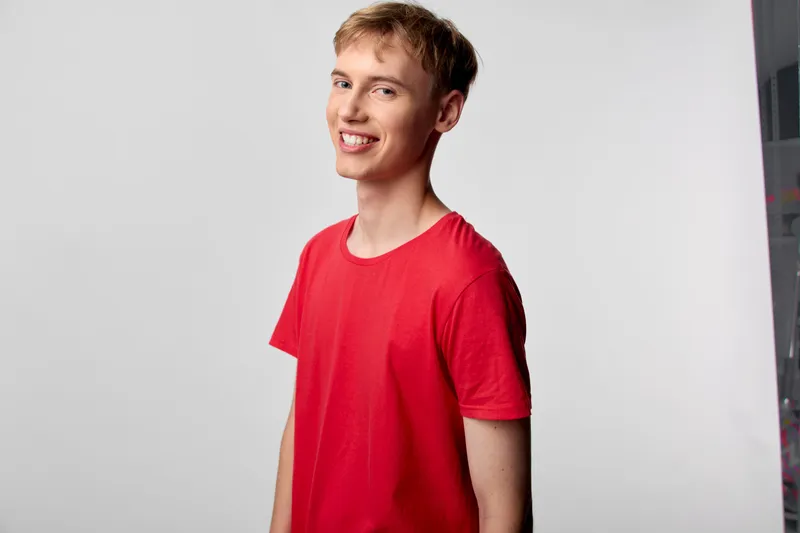 Man, smile, red shirt, casual style in a bright studio setting with a clean backdrop and warm lighting, showcasing a cheerful mood and modern lifestyle suitable for fashion and lifestyle use.
