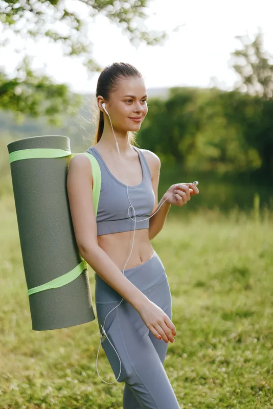 Young woman with a yoga mat enjoying a peaceful moment in nature, dressed in comfortable athletic wear, conveying a sense of health and wellness
