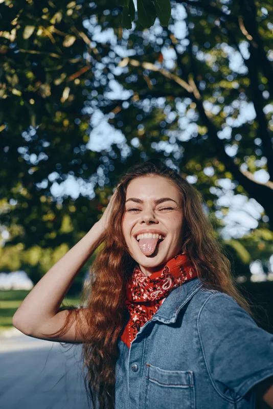 smiling woman with long hair wearing denim jacket and red bandana outdoors, joyful expression in sunny natural background