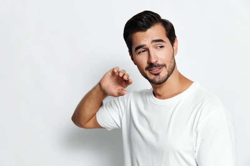 Handsome smiling man dressed in a casual white t-shirt, looking to the side with a playful expression on his face against a clean light background. Lifestyle concept.