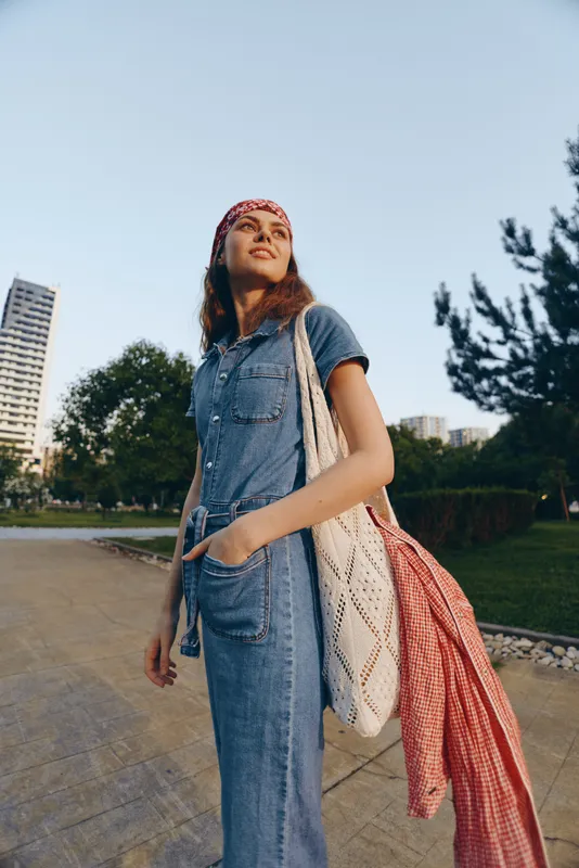 Lifestyle woman in modern boho-western denim street style wearing a headband and carrying a bag, standing confidently outdoors in film color light.