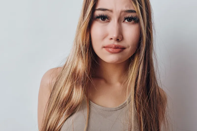 Young woman with long hair and sad expression looking at camera isolated on white background, emotional portrait and natural face closeup of female model.