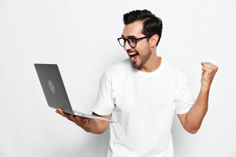Excited happy cheerful young man wear glasses celebrate success while hold laptop isolated on plain solid white background studio portrait. People lifestyle concept