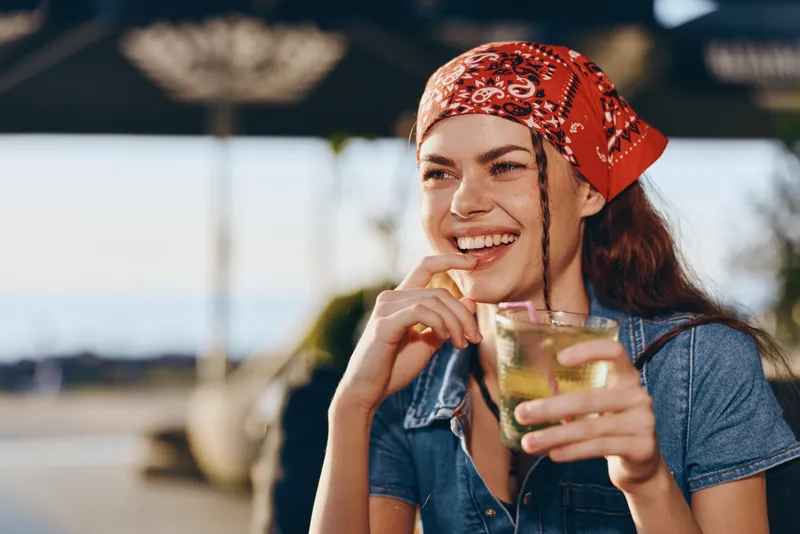 lifestyle woman in modern boho-western denim street style enjoying a refreshing drink outdoors with film color effect and warm natural lighting