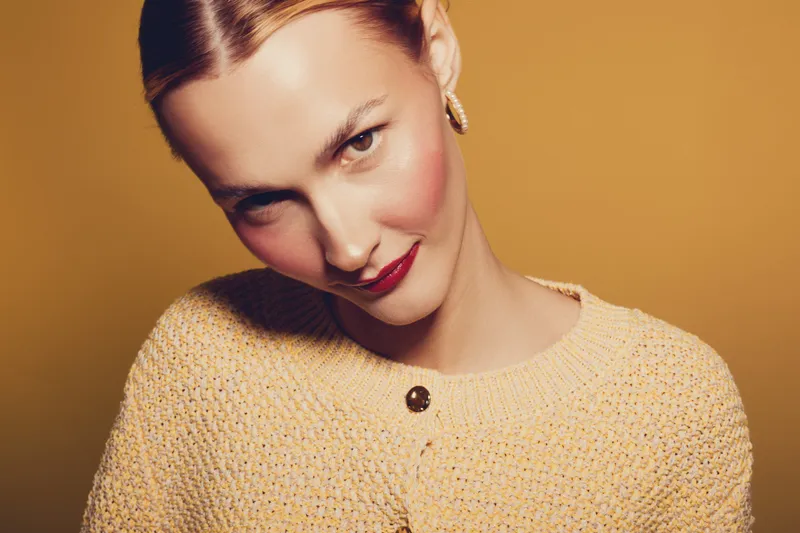 Young woman with fair skin and red lipstick wearing a yellow knitted sweater poses against a warm yellow background. Concept of fashion, beauty, and confident expression.